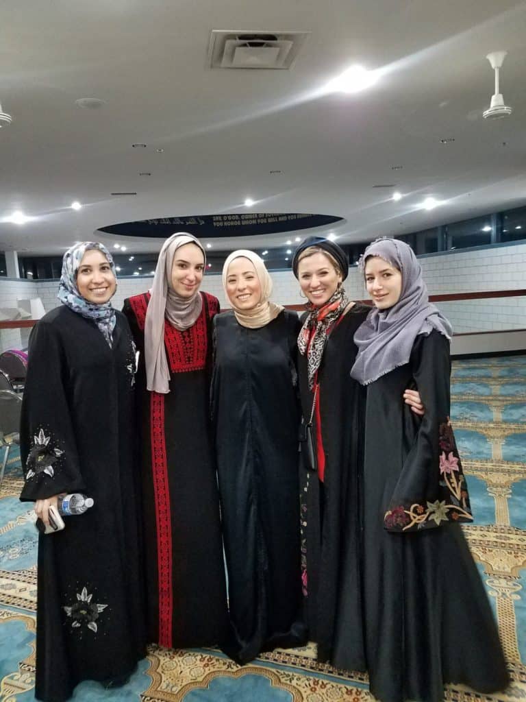 Five women smiling in traditional attire indoors.